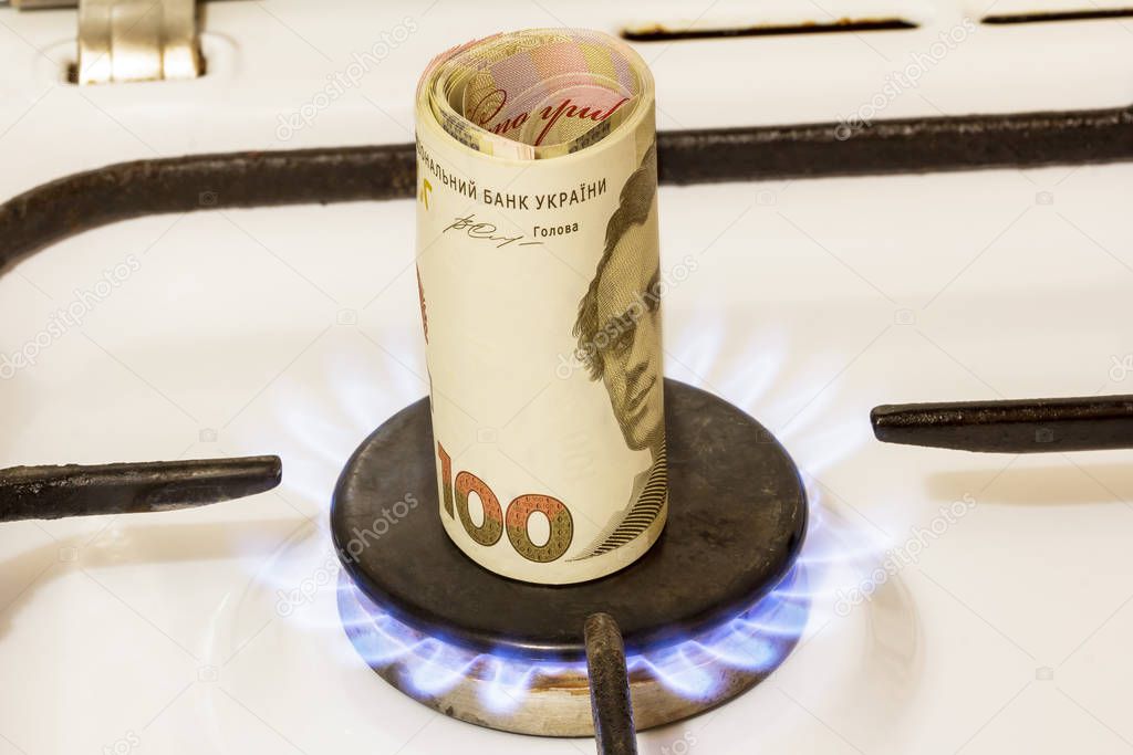 Stack of one hundred hryvnia notes on a gas stove in the center of gas comfort, gas burns.