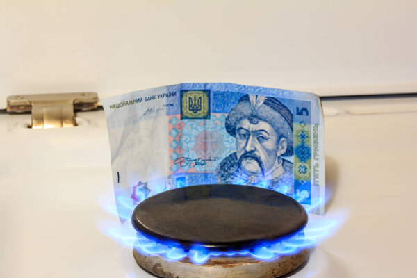 Gas burner, a fire burns, in the background five hryvnias. The concept of gas prices in Ukraine
