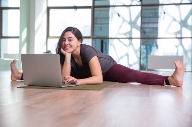 Evde dizüstü bilgisayarla yoga yapan genç bir kadının fotoğrafı. Güzel kız sınıfta yoga yapıyor. Yoga stüdyosu eğitmeni. Bulanık arkaplan