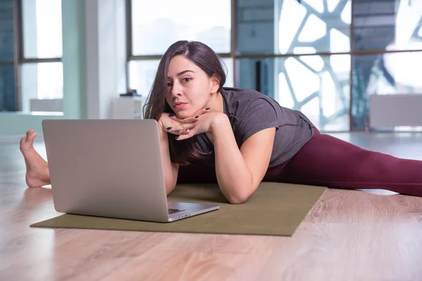 Photo de jeune femme pratiquant le yoga avec ordinateur portable à l'intérieur. Belle fille pratique le yoga en classe. Professeur de yoga studio. Fond flou — Photo