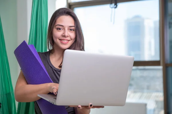 Retrato de jovem mulher de ioga com laptop indoor. Menina bonita na aula de ioga. Instrutor de estúdio de ioga. Fundo desfocado — Fotografia de Stock