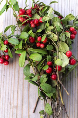 Juicy ,ripe berries of forest cranberries, gathered in a bouquet with branches and leaves, and lying on a wooden background.