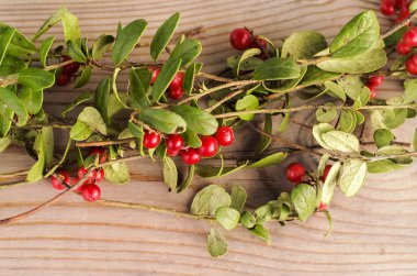 Red, round forest berries, on branches with leaves, lying on a wooden background.