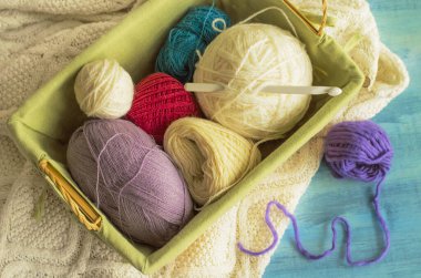 Üzerinde iplik ve kanca olan bir sepet örülmüş bir battaniye ve mavi bir masanın üzerinde duran leylak bir top..