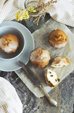 Pasta kağıdının üzerinde, gri-mavi bir kasede, bir bıçağın yanında, bir kavanozda duran hafif havlu ve kuru çiçeklerin yanında mermer desenli bir masanın arka planında duran pembe taze kahvaltı pastaları..