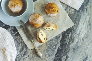 Kekler pasta kağıdının üzerinde ve gri-mavi bir kasede, bir bıçağın yanında, hafif bir havlunun yanında mermer desenli bir masanın arka planında yatıyorlar..
