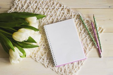 Beyaz bir peçetenin üzerinde beyaz laleler ve açık ahşap bir masa. Not defterinin ve kalemlerin yanında..