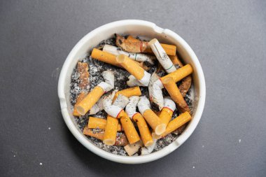 Sigaralar kül tablasında masanın üstünde. Orta pozisyon. Kötü sağlık, tehlike.