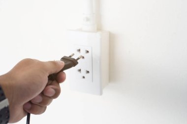 Kahverengi derili adamın sol eli elektrik prizine bağlı..