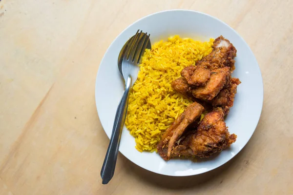 Top view Muslim yellow rice with fried chicken in white dish on light brown wooden background. Halal Food in Thailand. simply and local food.