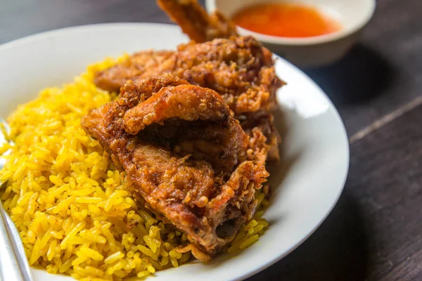 Close up Muslim yellow rice or Biryani rice with fried chicken and chicken sauce in white dish on brown wooden.Halal Food in Thailand