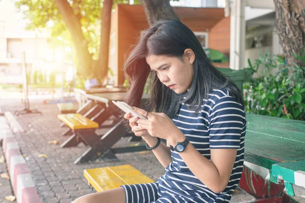Asian women tan skin with mobile phone in the park. she look happiness. task concept. Phone addict concept. Outdoor work. Free time concept. Copy space. Stress and serious concept.