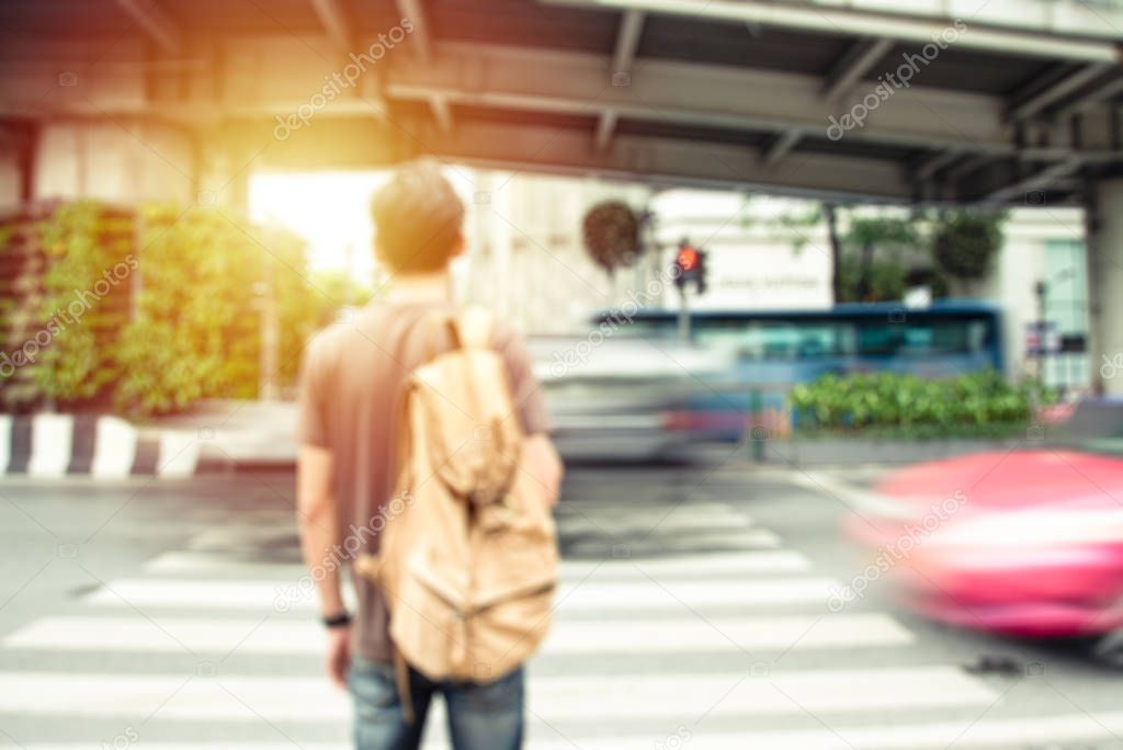 Defocus Back of Young male traveler traveling backpacker beside road with Blurry car on the way background. He waiting Cross the road. Vintage Tone and Selective Soft Focus. Travel and journey concept