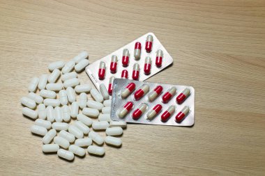 Different tablets and capsules , pills in foil blister packs, medications drugs on wooden background  