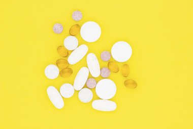 Vitaminler, haplar ve haplar. Sarı arka planda farklı vitaminler, haplar ve kapsüller..
