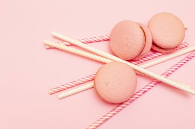 Taze pembe badem kurabiyeleri ya da badem kurabiyeleri. İçecekler için kağıt boruların etrafında. Fotokopi alanı olan pembe bir arkaplanda.