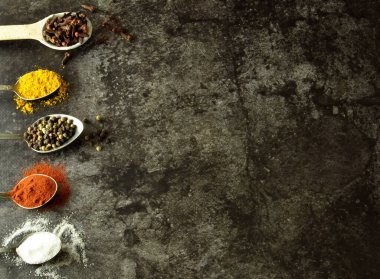 Karanlık bir arka planda kaşıklarda çeşitli baharatlar ve otlar. Yazmak için boş alan ya da yemek tarifleri.