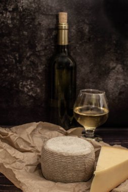 Kraft kağıdında peynir, bir şişe ve siyah bir arka planda beyaz şarap.