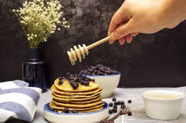 Bal, tahta kaşıktan krepe akar. Elindeki bal için tahta kaşık. Böğürtlenli krep ve bir tabakta bal.