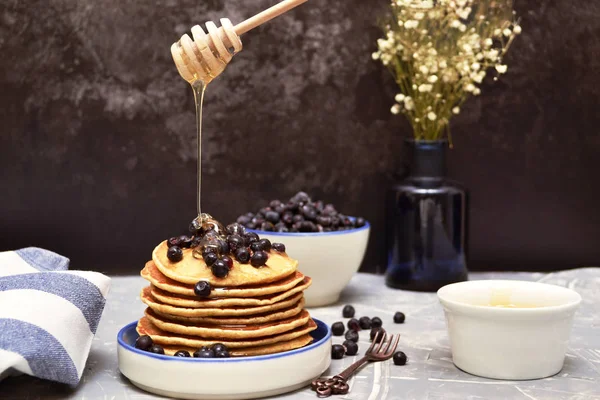 Pancakes with blueberries and honey on a plate. Honey flows from a wooden spoon.