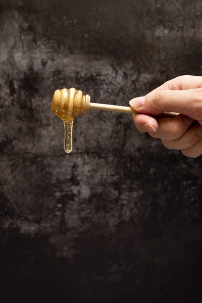 A drop of fresh honey flows down. A long drop of honey is hanging on a wooden spoon.