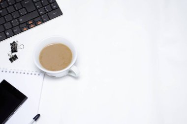 Beyaz bir masada bir klavye, defter, telefon, kalem ve kahve bulunur. Kayıt için kopyalama alanı var