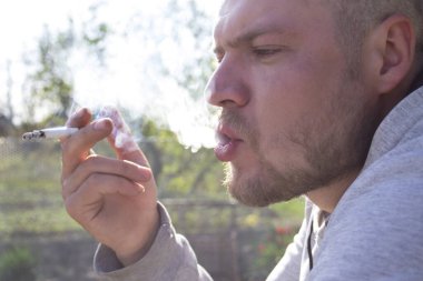 Genç adam bir sigara içiyor ve kalın bir duman çıkarıyor.