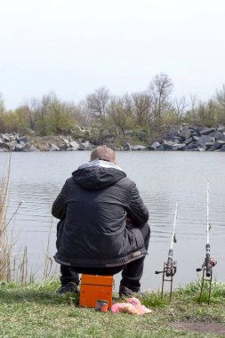 Bir adam göletin kıyısında balık yakalar. Bir balıkçı bir balıkçı oltaya oturur ve iki dönen çubuğun yanına..