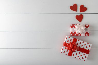 Kurdeleli hediye kutuları ve beyaz ahşap arka planda kalpler. Üst görünüm