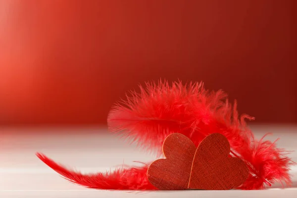 Corações de madeira com plumagem sobre fundo vermelho. Fundo romântico — Fotografia de Stock