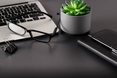 Dizüstü bilgisayarı, not defteri, küçük sulu aksesuarları ve koyu gri arkaplanı olan minimum iş yeri. Seçici odak