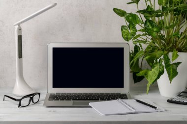 Üzerinde açık bir defter, bir bitki, bir defter ve ahşap masa üzerinde kırtasiye malzemesi olan bir işyeri. Evde ya da ofiste.. 