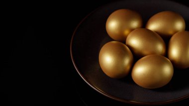 Paskalya, koyu kahverengi bir tabakta altın doğal yumurtalar boyadı. Kopyalama alanı olan siyah arkaplan