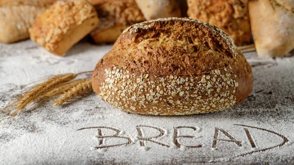 在散落的面粉上放了一大块刚烤好的多粒面包 带有Bread字的轻背景 — 图库照片