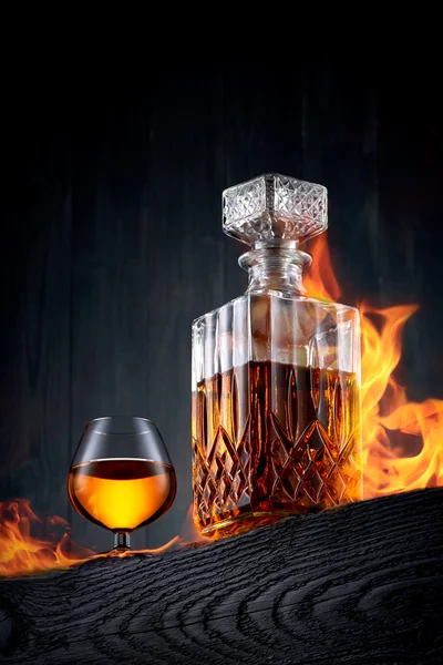 Queima de garrafa e copo de uísque em uma mesa de madeira preta — Fotografia de Stock