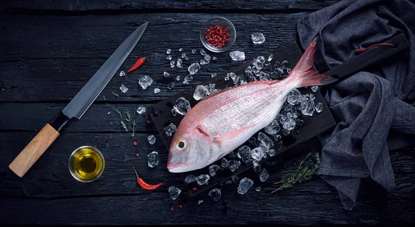 Pescado fresco de dorada española (breca) sobre hielo sobre una mesa de madera negra — Foto de Stock