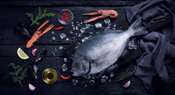 Peixe-dourado fresco (sargo) e frutos do mar na aba preta de madeira — Fotografia de Stock