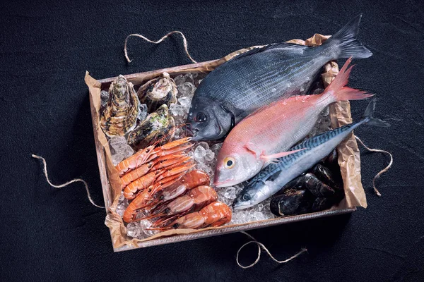 Peixes e frutos do mar frescos espanhóis em caixa de madeira sobre mesa de pedra preta — Fotografia de Stock