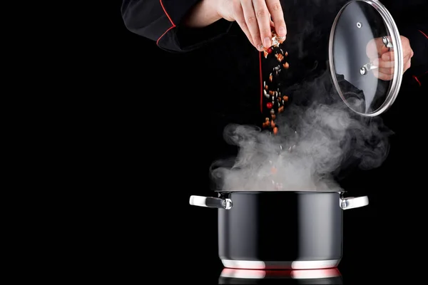 Moderner Koch in Berufskleidung würzt dampfenden Topf — Stockfoto