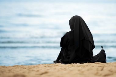 Sahilde oturan siyah giysileri ile Müslüman kadın
