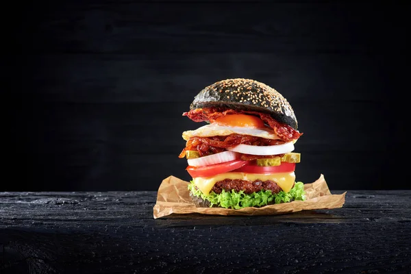 Czarny burger z jajka i boczek na drewnianym stole — Zdjęcie stockowe