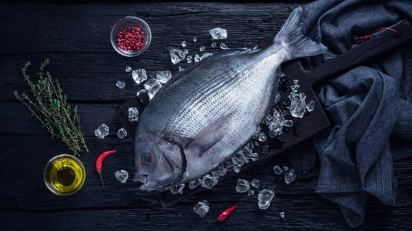 Pescado blanco fresco (sargo) sobre hielo sobre una mesa de madera negra — Foto de Stock