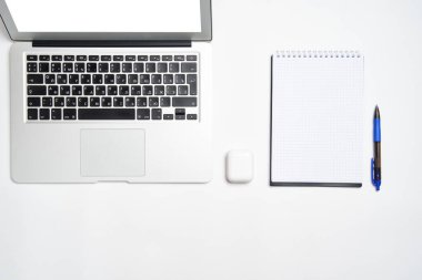 Bilgisayarlı çalışma alanı, beyaz arka planda kalem ve kablosuz kulaklıklı Not Defteri. Yukarıdan manzara. Düz biçim.