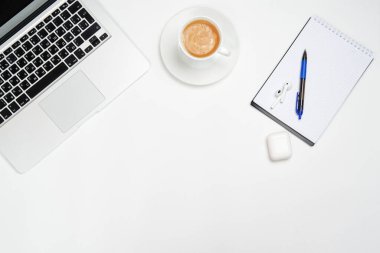 Bilgisayarlı çalışma alanı, beyaz arka planda kalem ve kablosuz kulaklıklı Not Defteri. Yukarıdan görünüşü.