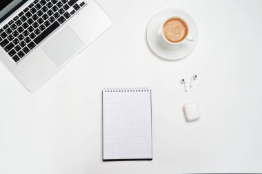 Bilgisayar, kalem ve kablosuz kulaklıklı Not Defteri, beyaz arka planda. Yukarıdan bak. En az çalışma alanı