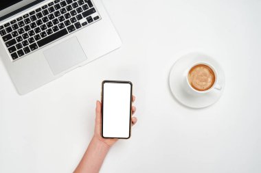 Akıllı telefon tutan kadının en iyi görüntüsü. Laptop ve bir fincan kahveyle çalışma alanı