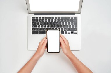 Kız, dizüstü bilgisayarının üzerinde, izole edilmiş beyaz bir arka planda akıllı telefon tutuyor.