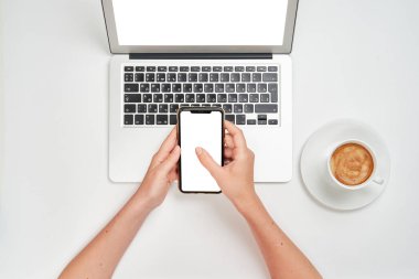 Üst Manzara. Kız elinde bir akıllı telefon tutuyor ve diğer eliyle ekranda basıyor. İzole edilmiş beyaz bir arkaplanda işyeri