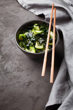 Salata, salatalık dilimli çiğ deniz yosunu ve koyu gri arka planda susam.