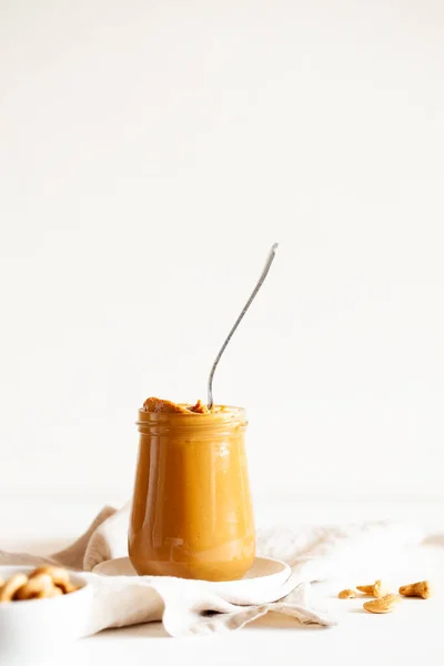 Homemade natural paleo nut peanut cashew creamy butter in glass jar and spoon on white background — 스톡 사진